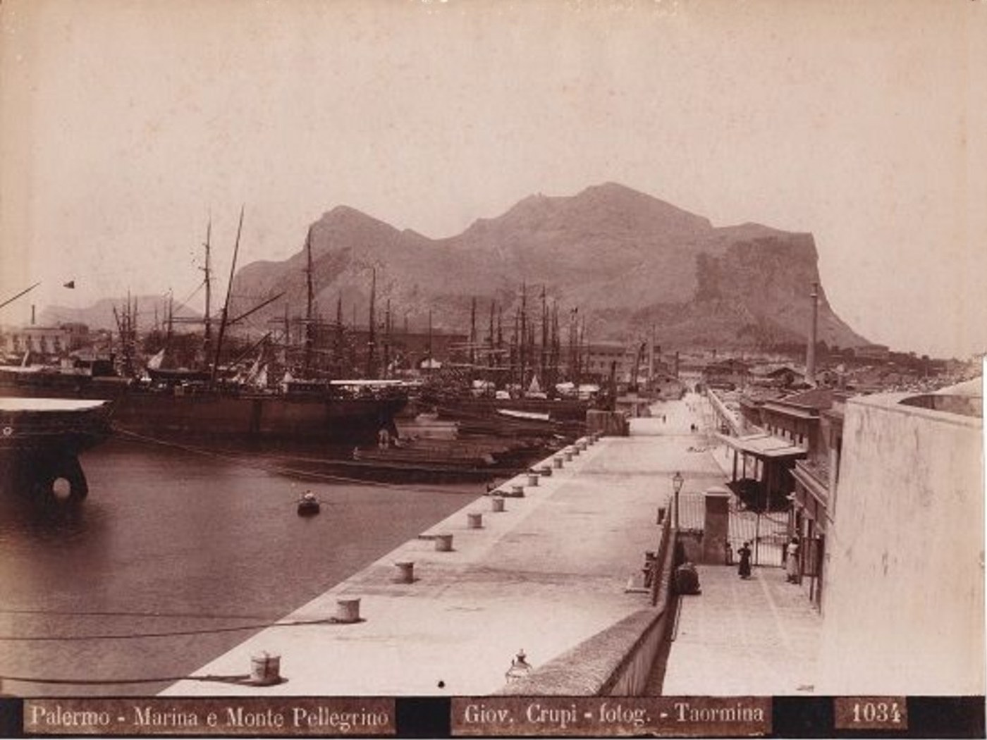 Старая фотография в сепии: гавань с парусными судами у причала, вдоль набережной уходит мощёная улица, на заднем плане та же скалистая гора; внизу на паспарту напечатана подпись Palermo — Marina e Monte Pellegrino