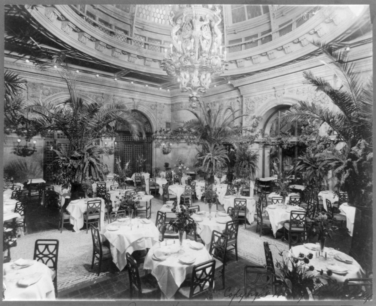 Ресторанный зал Palm Garden отеля Waldorf-Astoria с пальмами и накрытыми столами
