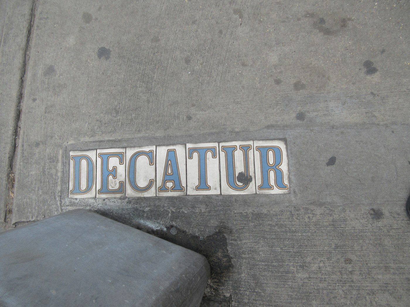 Плиточная надпись DECATUR синими буквами на белых изразцах, вмонтированная в серый бетонный тротуар